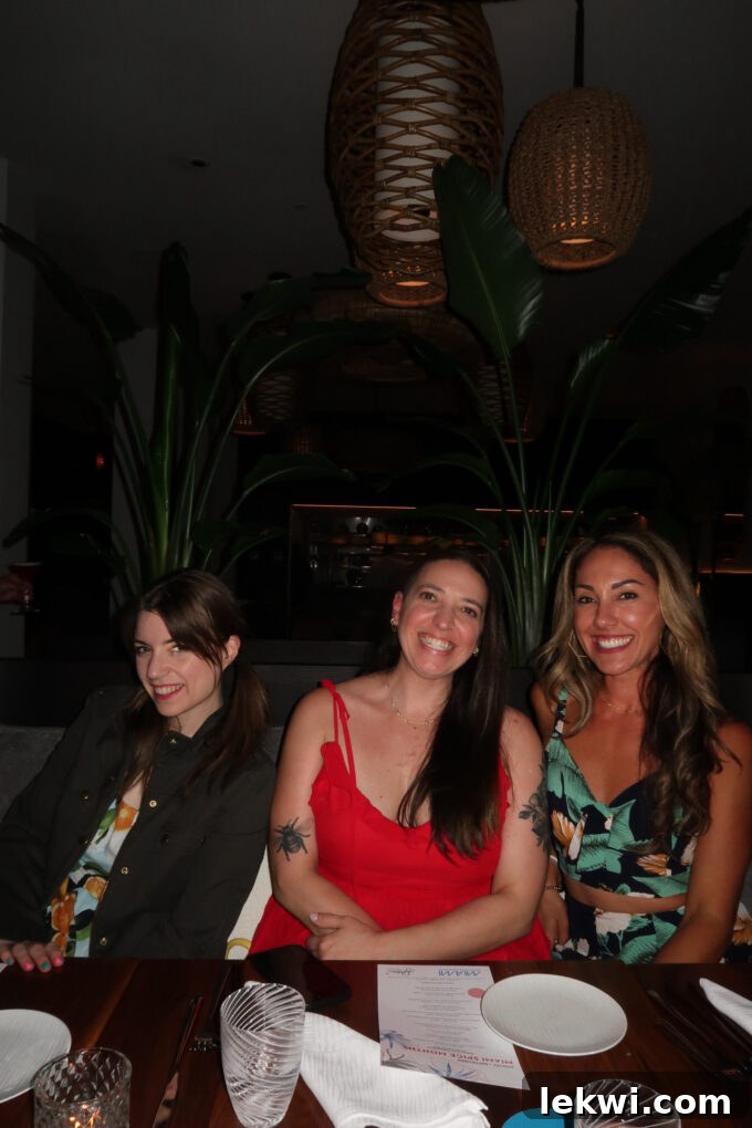Three food bloggers smiling warmly in a dimly lit, elegant restaurant setting, captured during a relaxed moment of the nine-course dinner.