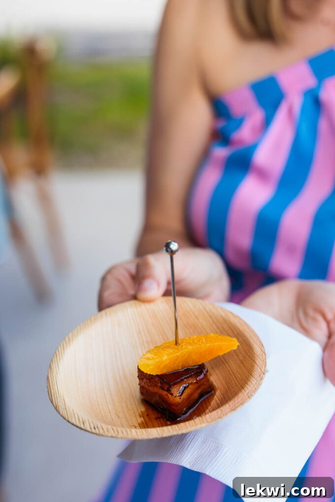 A beautifully plated pork belly and orange appetizer in a bowl with a skewer, showcasing the gourmet presentation of the welcome happy hour food.