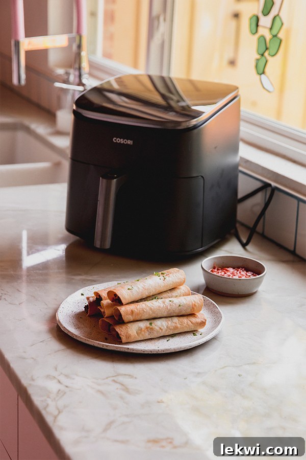 Veggie pizza rolls stacked on a plate with an air fryer in the background.