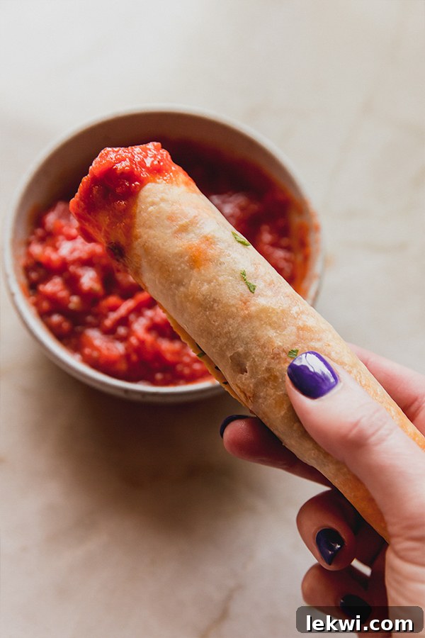 Veggie pizza rolls being dipped into pizza sauce.