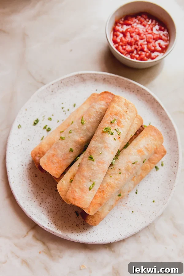 Veggie pizza rolls stacked on a plate topped with chopped parsley with sauce on the side in a bowl.