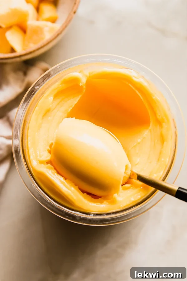 Scooping a vibrant mango Ninja Creami sorbet from its container, showing its thick and creamy texture.