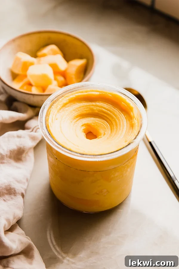 Vibrant mango Ninja Creami sorbet in its container, with a bowl of frozen mango chunks in the soft-focus background.