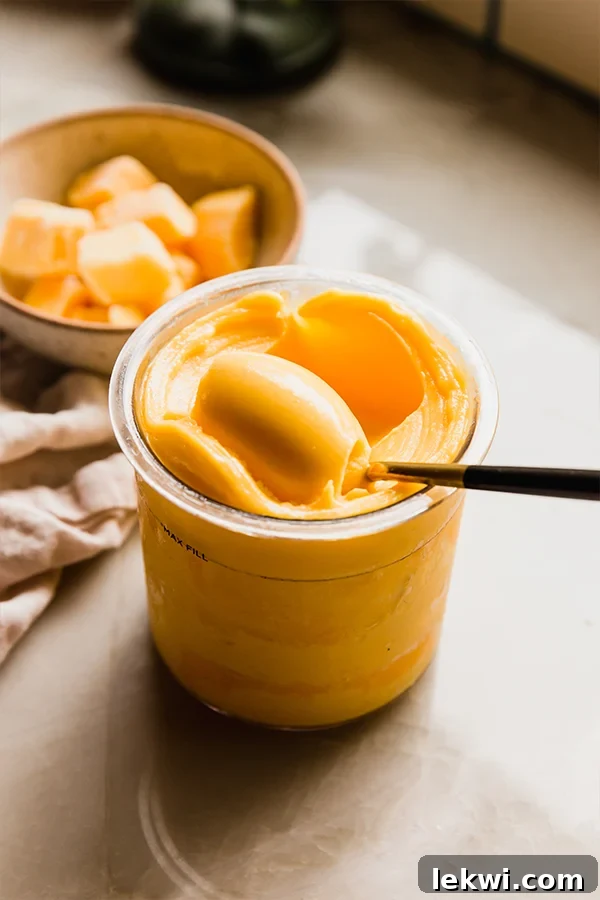 Scooping creamy 2-ingredient mango sorbet from a Ninja Creami pint, with a bowl of fresh mango in the background.
