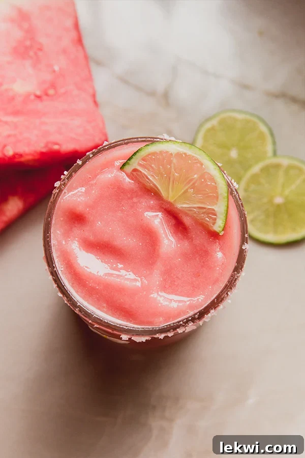 Frozen watermelon margarita mocktail in a glass with a salted rim and topped with a slice of lime, and more lime slices on the side.