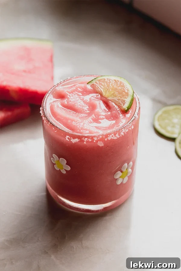 Frozen watermelon margarita mocktail in a glass with a salted rim and topped with a slice of lime.