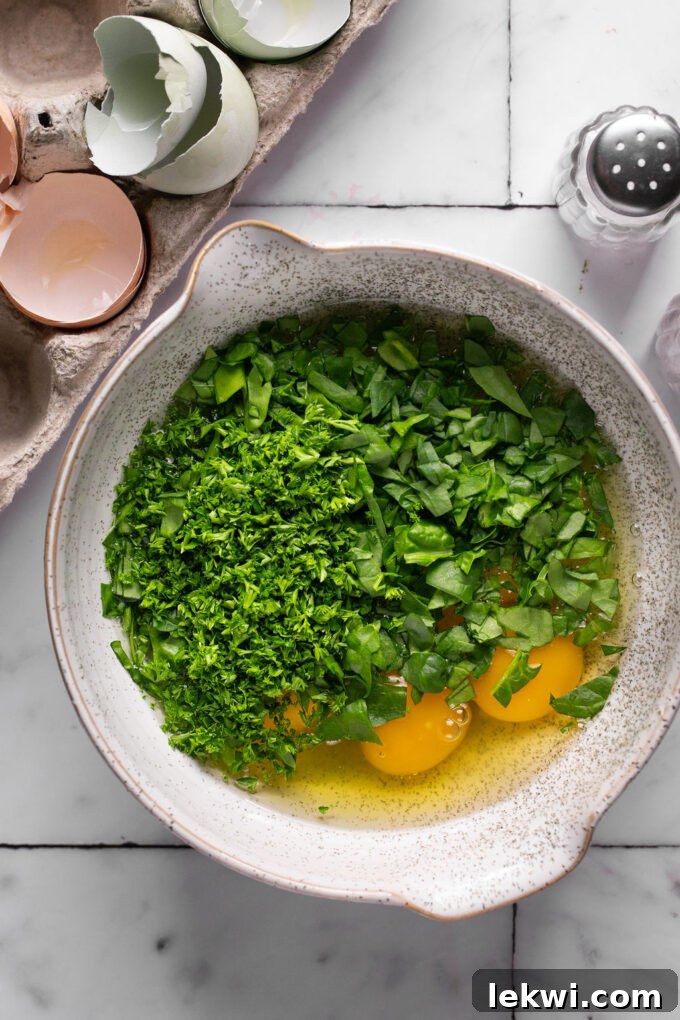 Unwhisked eggs with spinach and parsley in a large mixing bowl, before combining.