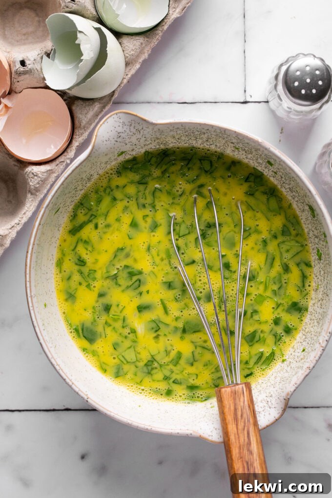Eggs, spinach, and parsley fully whisked and combined in a bowl, ready for baking.