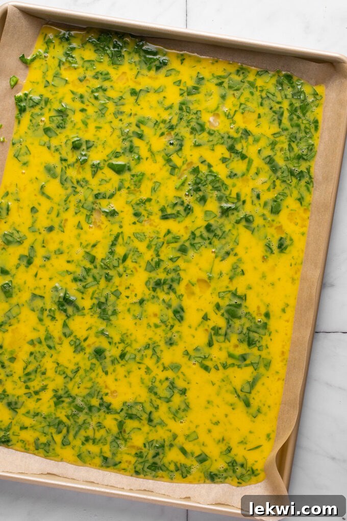 Egg and spinach mixture freshly poured onto a parchment-lined baking sheet, ready for the oven.