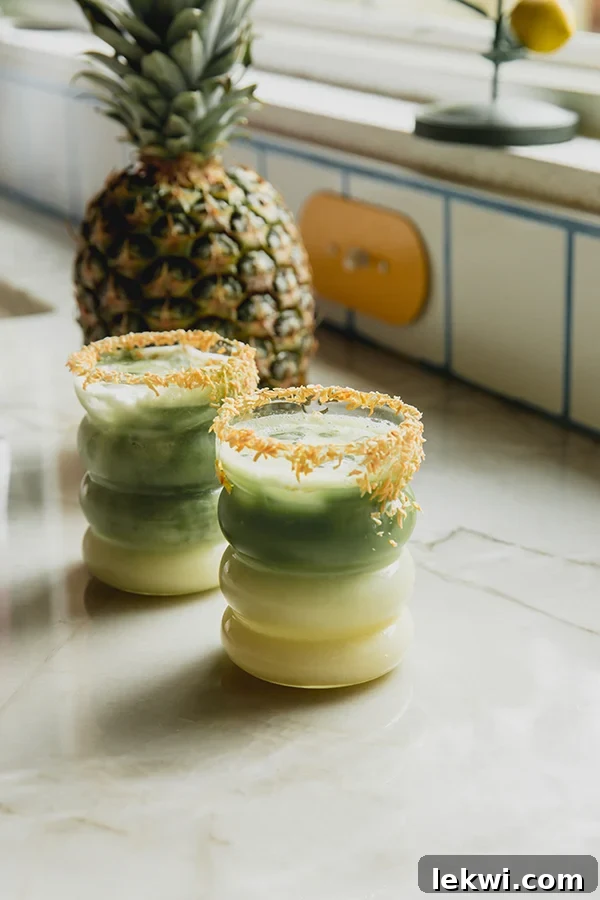 Two matcha pina coladas with a toasted coconut rim, with a whole pineapple in the background.
