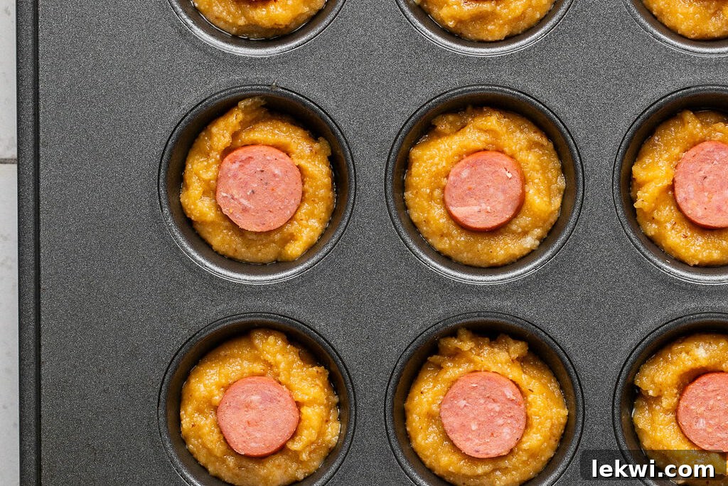 Unbaked corn dog muffins in a mini muffin tin, showing the hot dog slices perfectly nestled in the batter.