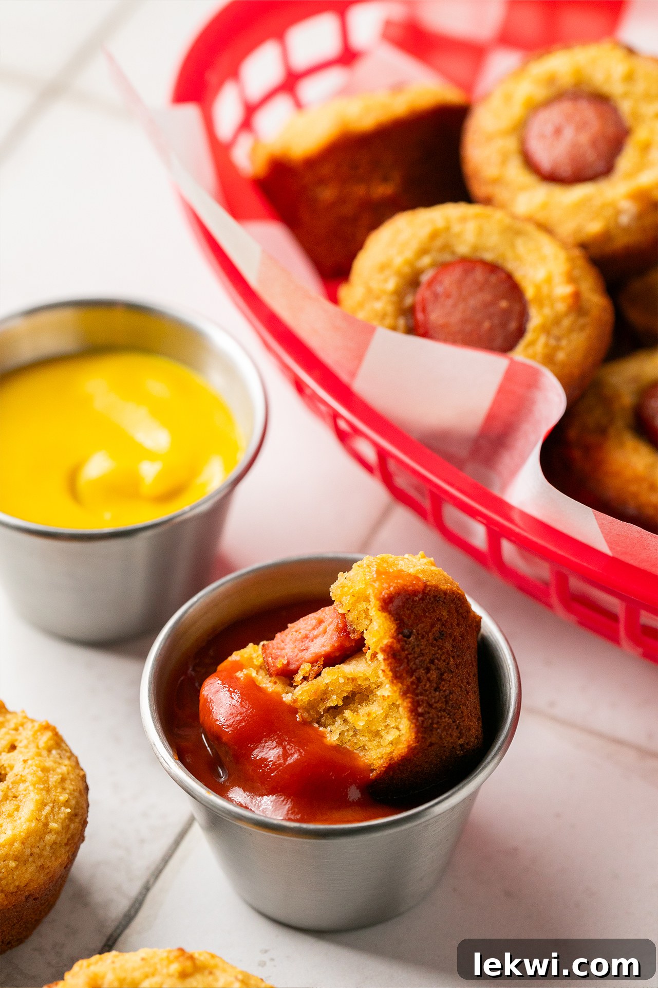 A corn dog mini muffin being dipped into a small bowl of ketchup, highlighting its golden texture and inviting presentation.