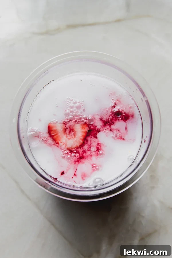 Fresh strawberries, carton coconut milk, white grape juice, and cranberry juice combined in a Ninja Creami container, ready for freezing.