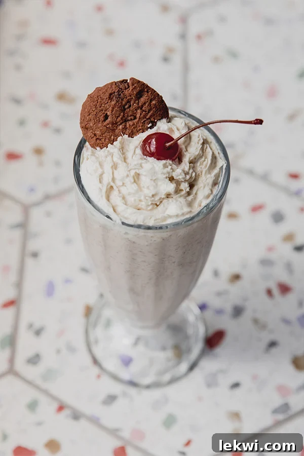 Ninja Creami milkshake topped with whipped cream, a cookie, and a cherry, served in a tall glass.