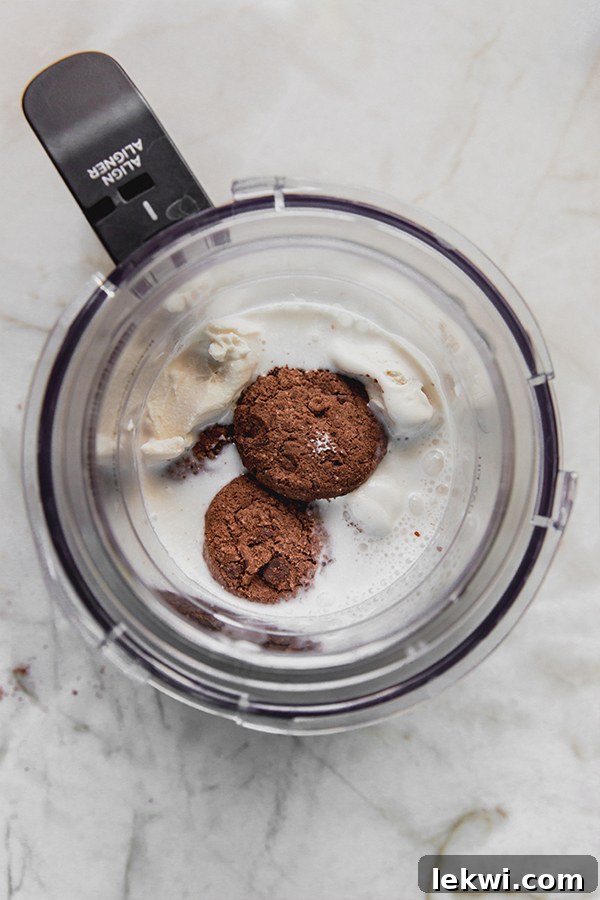 Almond milk, dairy-free ice cream, and gluten-free cookies in a Ninja Creami cup before blending.