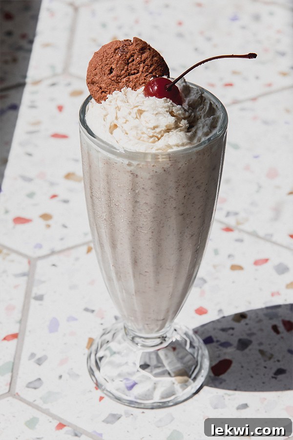 Close-up of a Ninja Creami milkshake topped with dairy-free whipped cream, a whole cookie, and a cherry.