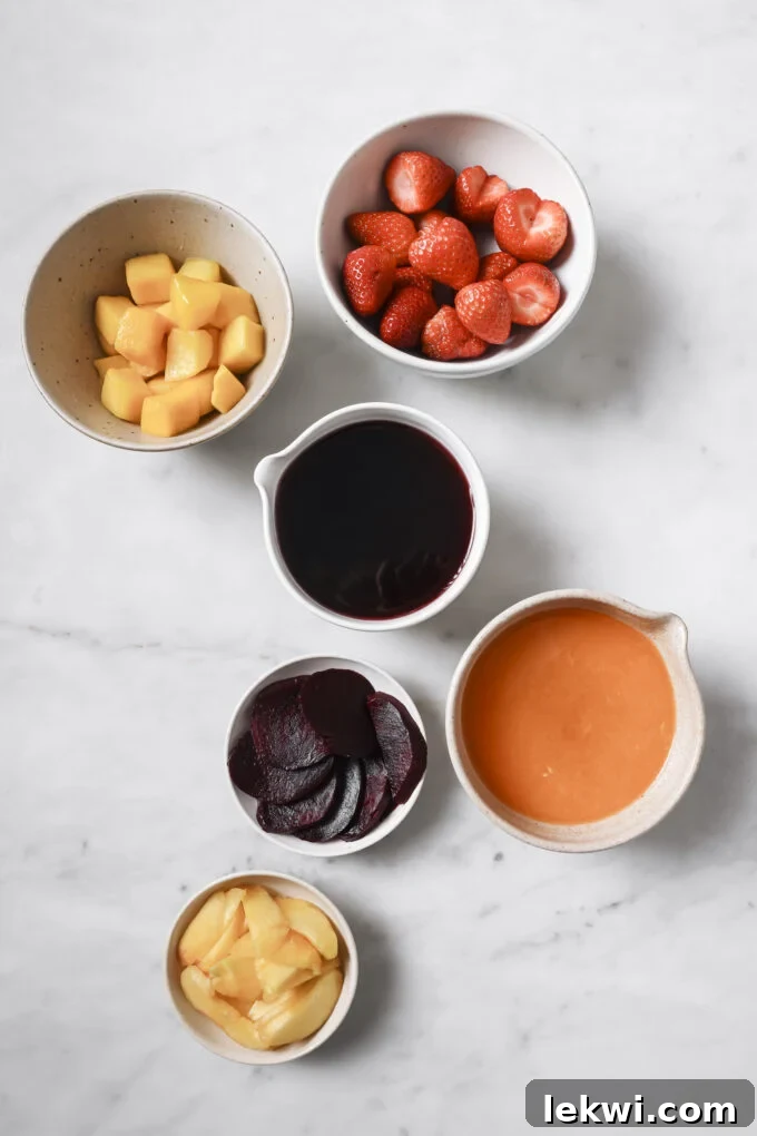 Separate bowls of fresh fruit and veggie freezer pop ingredients including strawberries, beets, mango, and peaches, ready for blending.