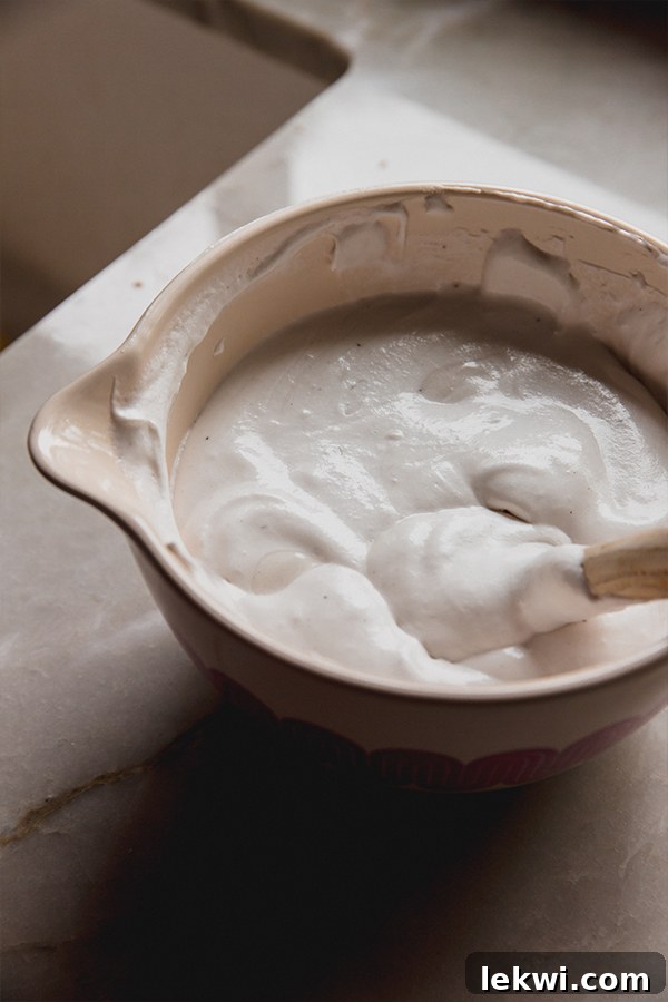 Creamy vanilla pudding being thoroughly mixed with a spatula in a large, transparent glass mixing bowl, showcasing its smooth texture.