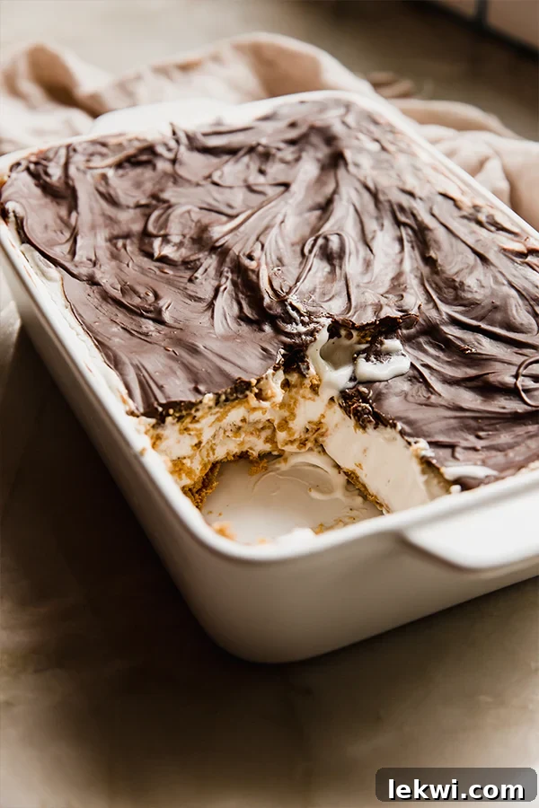 A large, rectangular gluten and dairy-free eclair cake resting in a baking dish, with a single, perfect slice already removed, showcasing the internal layers.