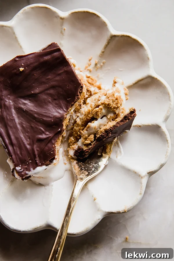 A slice of gluten and dairy-free eclair cake on a plate, with a fork cutting into it to show the multiple layers of cracker, pudding, and ganache.