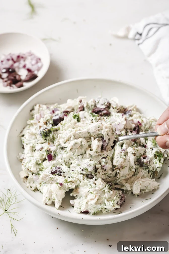 Tzatziki chicken salad in a bowl, topped with fresh herbs. A spoon is scooping a portion.
