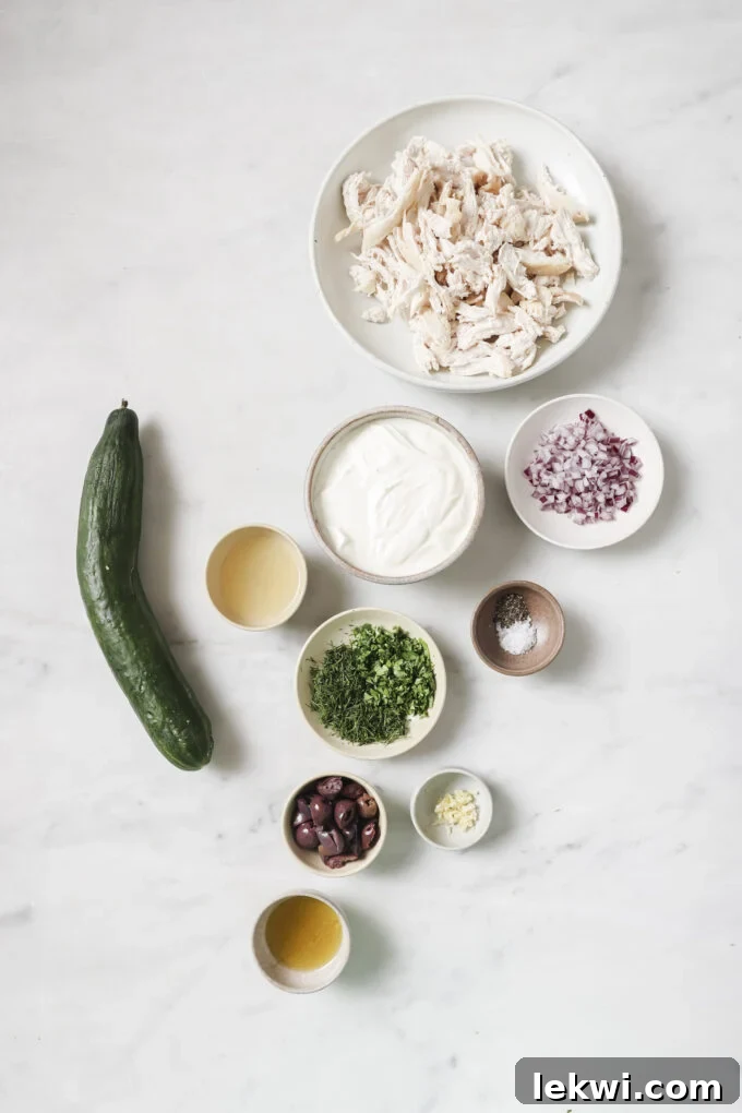 Ingredients for Tzatziki chicken salad laid out in separate bowls: cucumber, yogurt, herbs, chicken, olives, red onion.