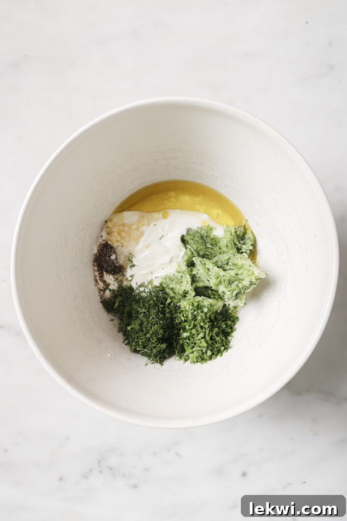 Shredded cucumber, herbs, yogurt and oil in a large white bowl.