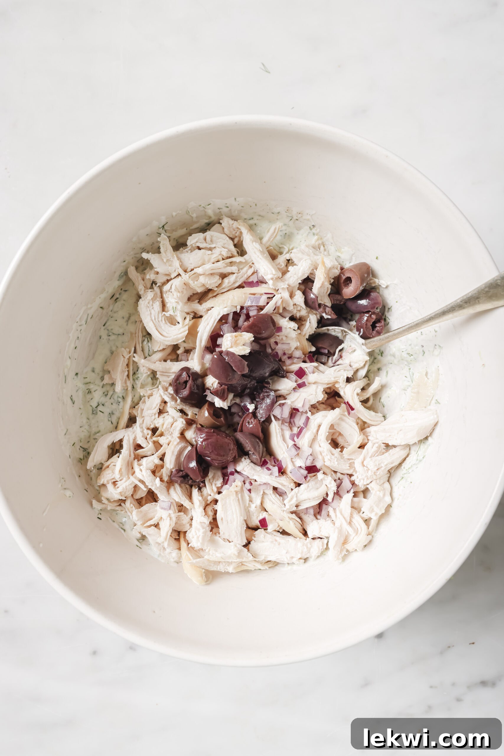 Shredded chicken, chopped olives and tzatziki unmixed in a bowl.