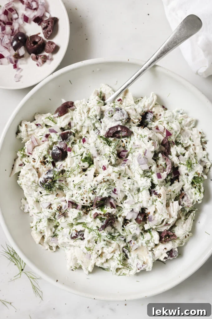 Tzatziki chicken salad in a bowl, topped with fresh herbs, with a spoon scooping in.