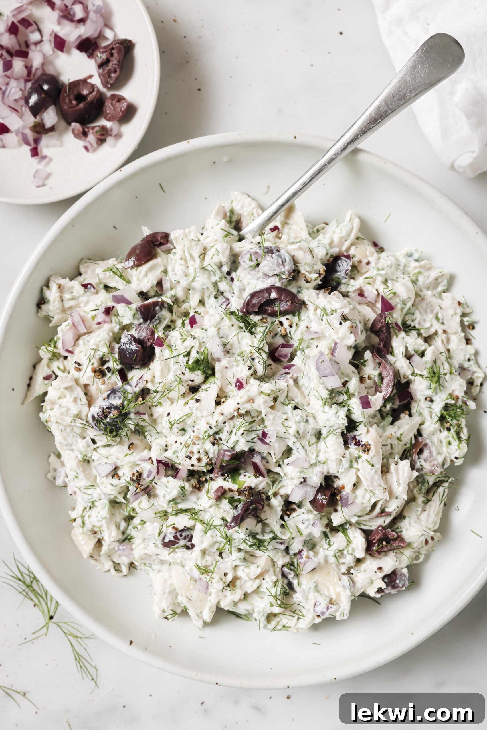 Tzatziki chicken salad in a bowl, topped with fresh herbs, with a spoon scooping in.