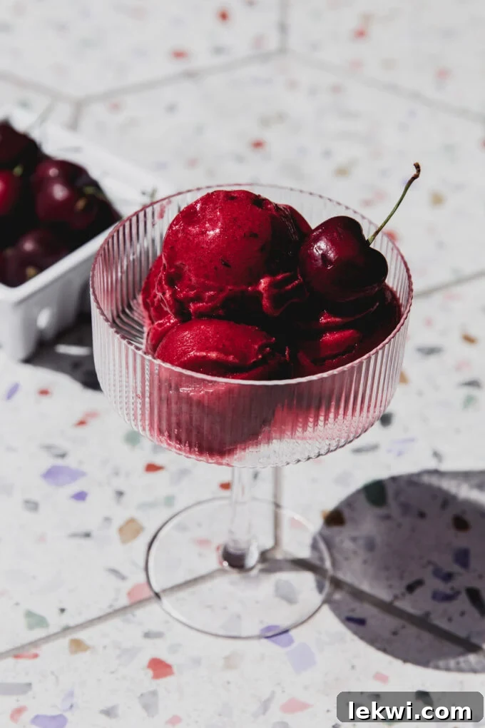 Cherry shirley temple sorbet scooped into a serving glass, topped with a fresh cherry.