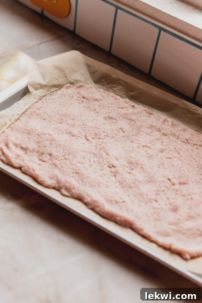 Flattened ground chicken on a lined baking sheet.