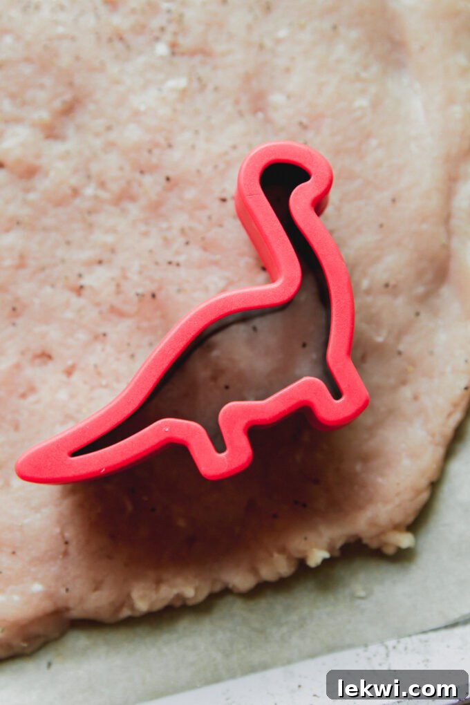 Red dinosaur-shaped cutter on flattened ground chicken.