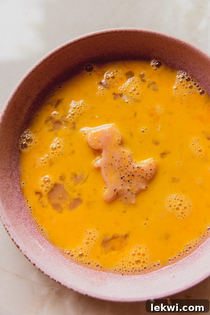 Dino-shaped chicken in a bowl of egg wash.