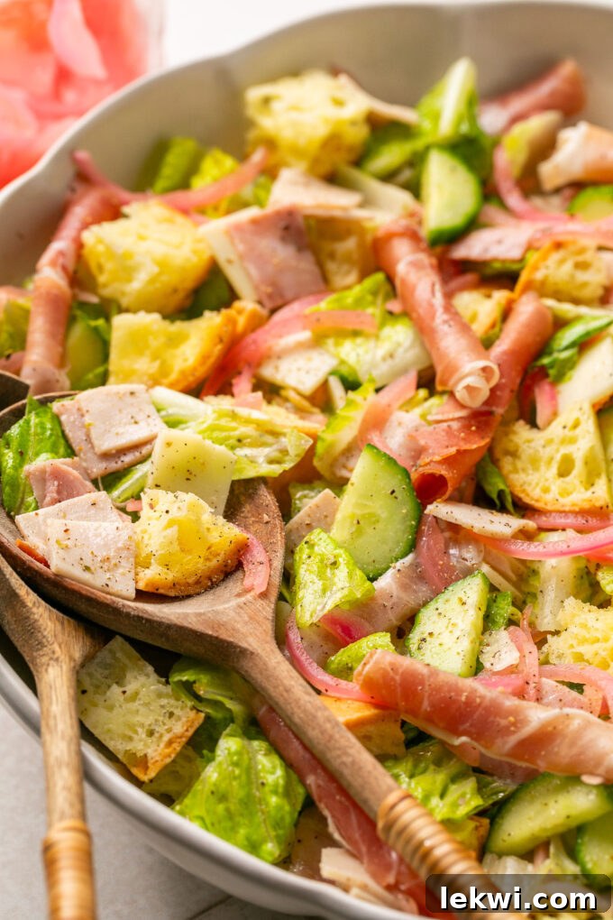 A serving spoon taking a spoonful of the sub in a tub salad, showing the mixed ingredients.