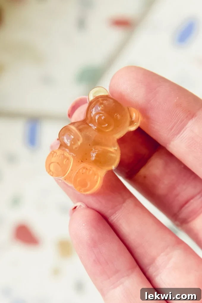 A close-up shot of an apple cider vinegar gummy bear being held gently between two fingers, highlighting its soft texture and inviting appearance.
