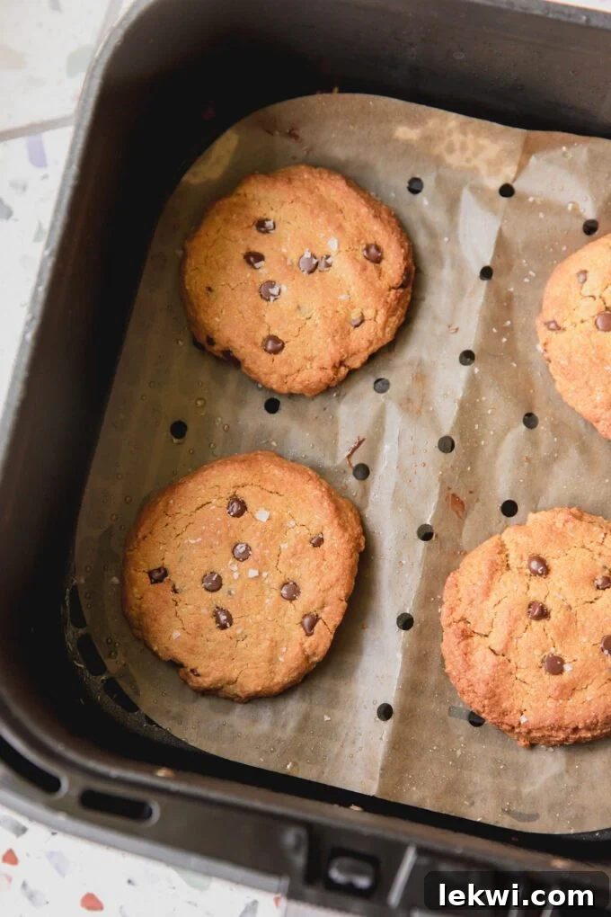 Air fryer chocolate chip cookies, fully cooked on parchment paper in the air fryer basket.