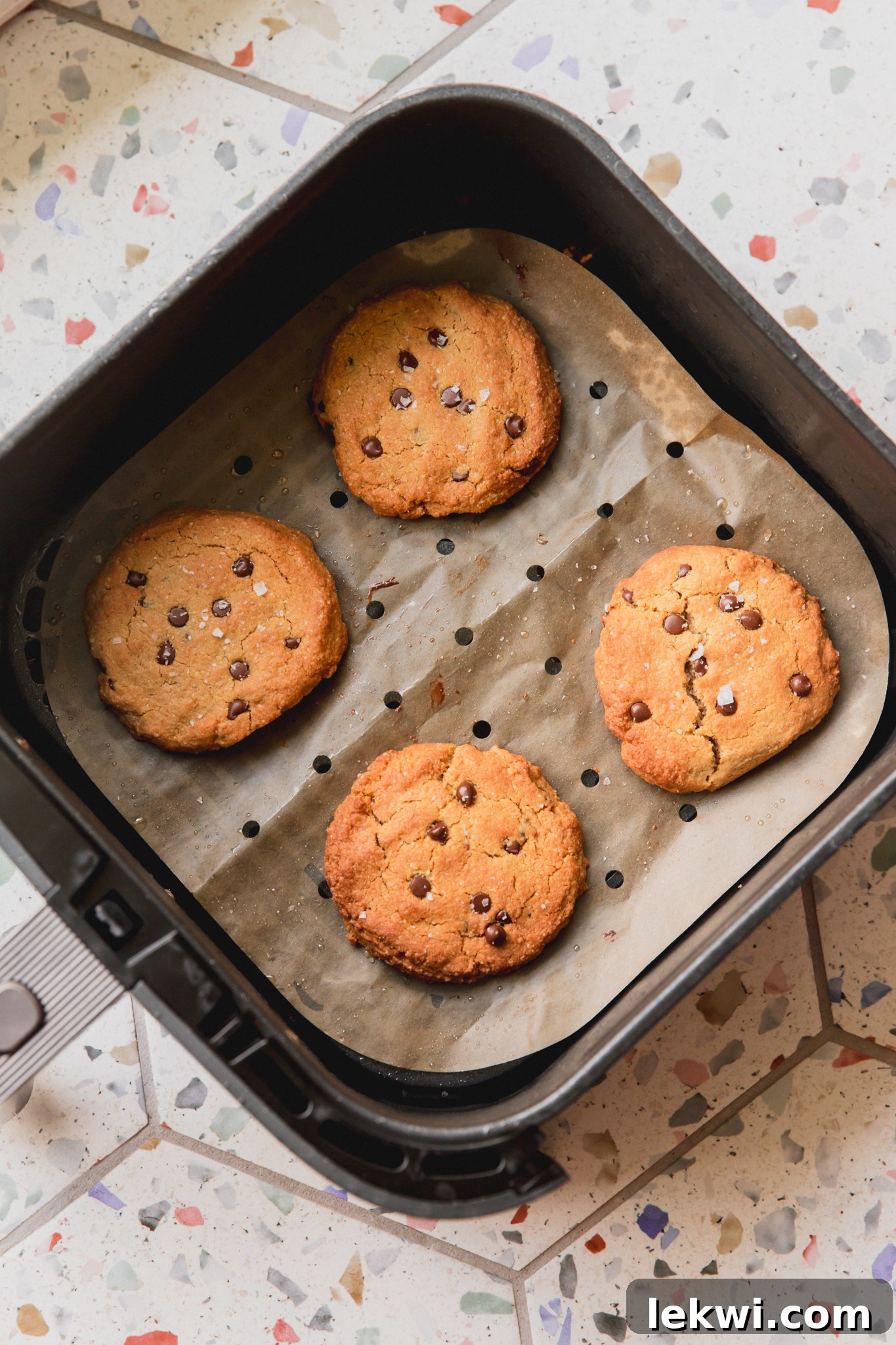 Air fryer chocolate chip cookies, fully cooked on parchment paper in the air fryer basket.