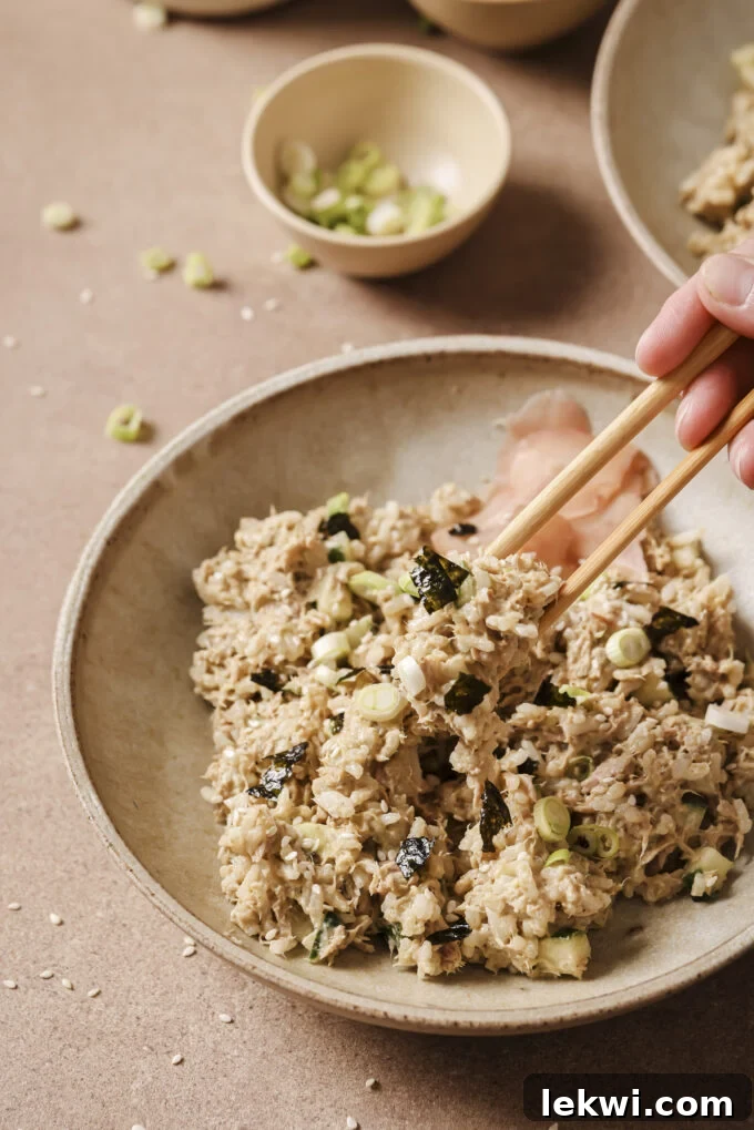 Chopsticks picking up a helping of avocado tuna rice from the bowl.