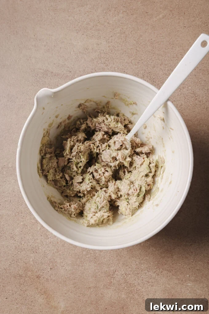 Avocado and tuna being mixed in a white bowl with a spoon.