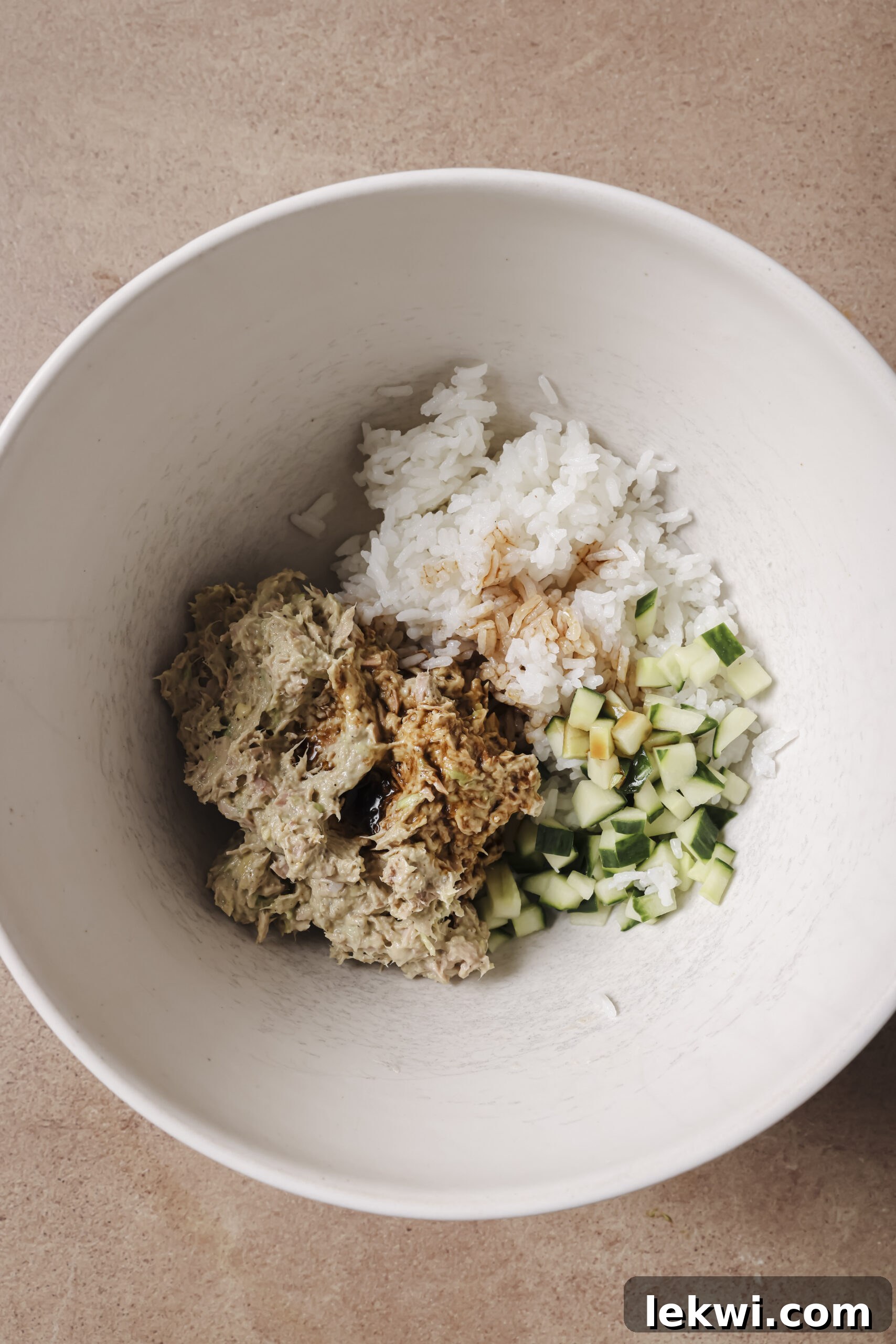 Avocado, tuna, rice and cucumber being mixed in a white bowl.