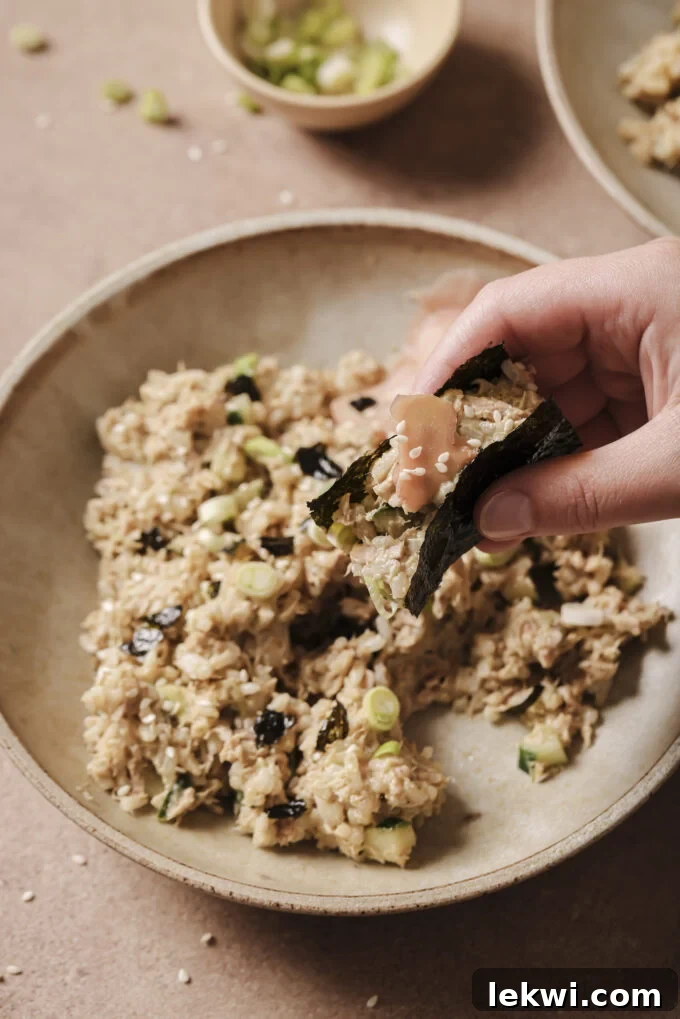 Avocado tuna rice bowl with a helping wrapped in seaweed being held over the bowl.