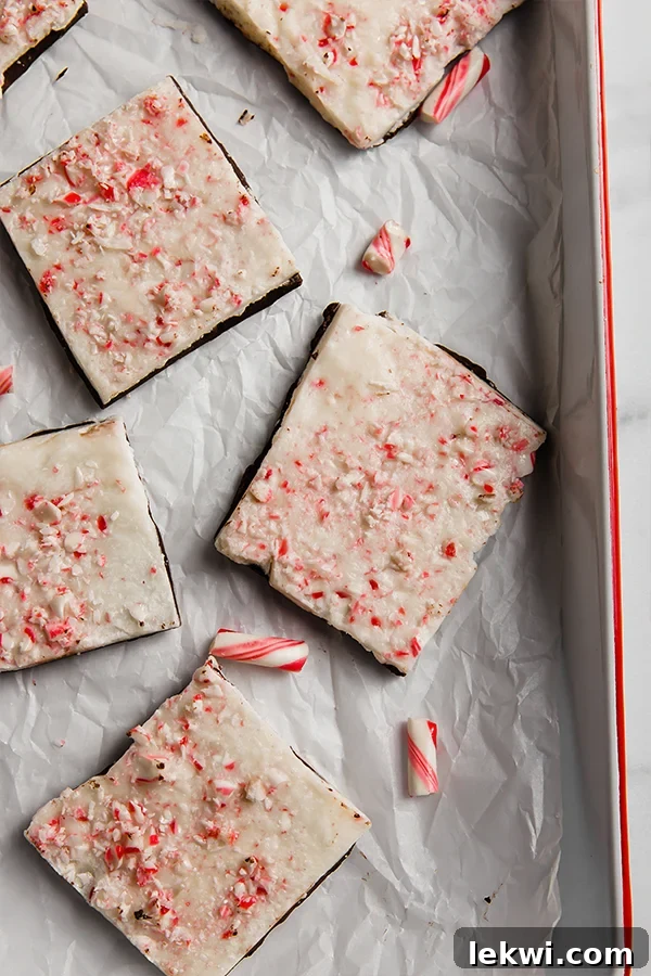 Lined baking dish filled with two layers of paleo peppermint bark, topped with crushed candy canes and pomegranate seeds, ready to be chilled.
