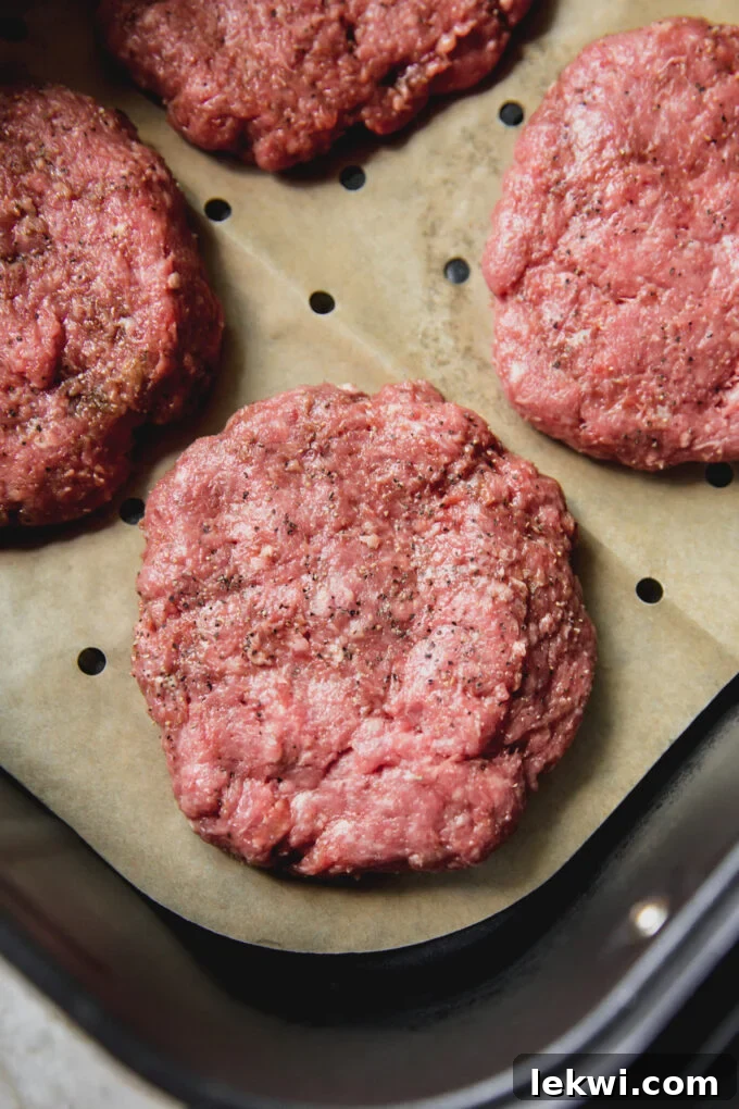 Air fryer burgers, lightly seasoned and uncooked in the air fryer with vented parchment paper.