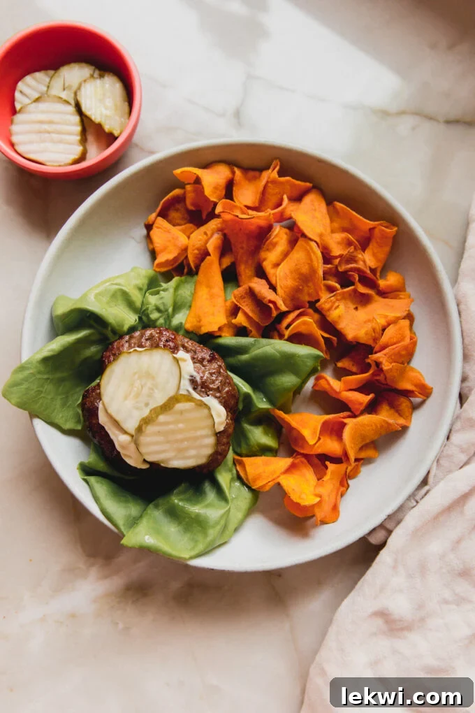 Air fryer burger on a lettuce wrapped, topped with mayo and pickles and paired with sweet potato chips. 