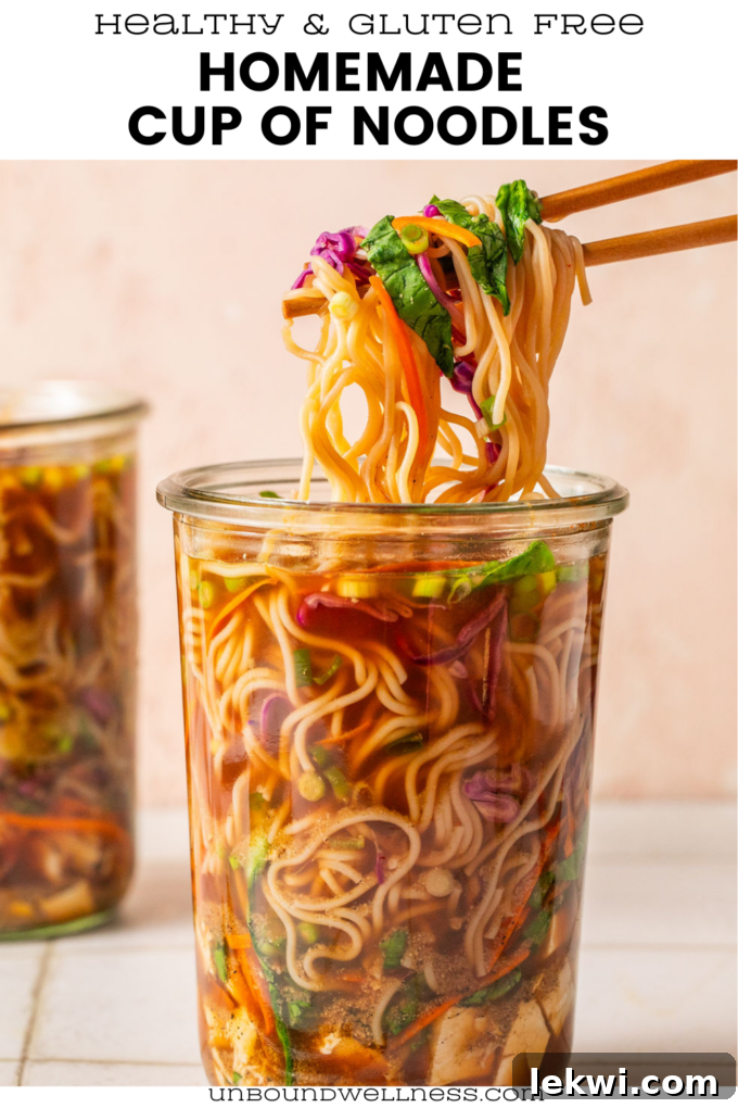 Homemade cup of noodles with ramen, veggies and broth in a glass jar with chopsticks pulling the noodles.