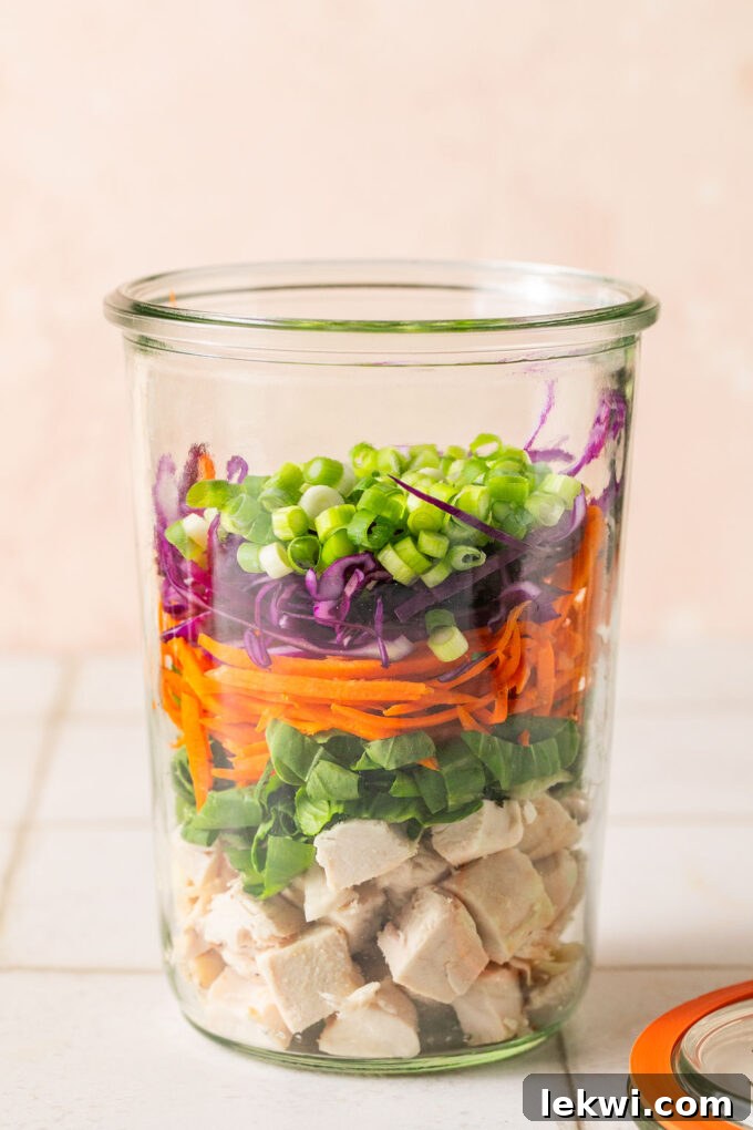 Cooked chicken, veggies, and green onion layered in a glass jar.