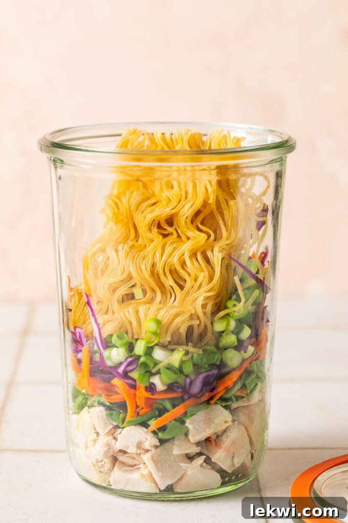 Cooked chicken, veggies, green onion and a brick of gluten free ramen layered in a glass jar.
