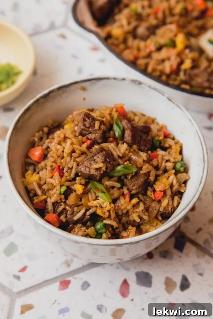 A vibrant bowl of homemade steak fried rice, garnished with fresh green onions, showcasing tender steak pieces, carrots, and peas.