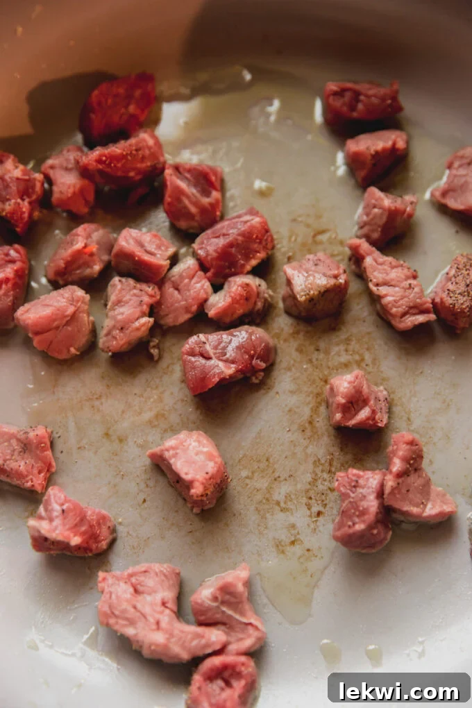 Cubed steak, raw cooking in a pan with oil, showing a nice sear.